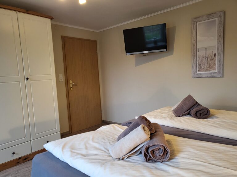 Schlafzimmer mit zwei Betten, Fernseher und Dekorationsbilder, ideal für Ferienwohnungen in Brake.
