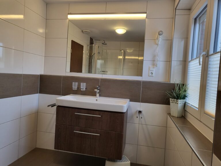 Badezimmer mit Waschbecken, Spiegel und Fenster in Ferienwohnung Brak.