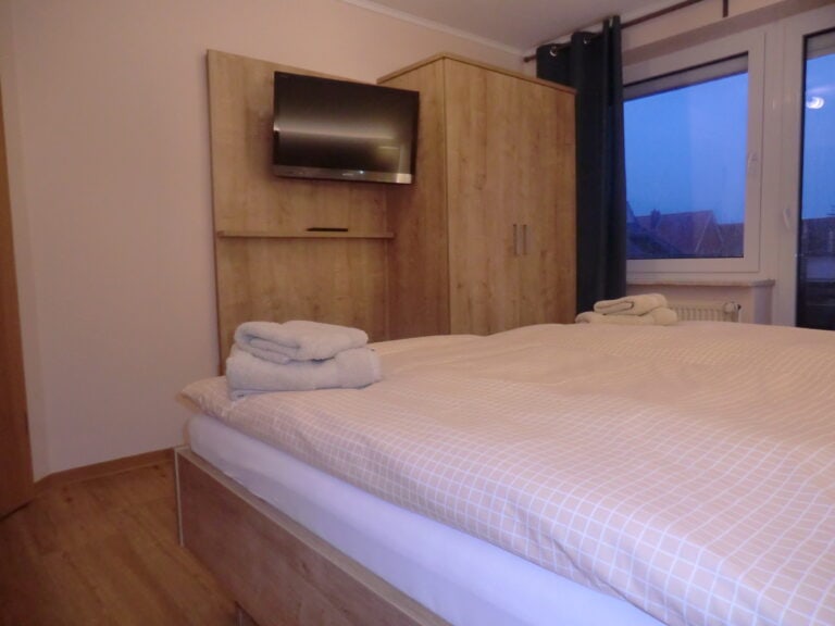 Schlafzimmer mit Doppelbett, TV und Blick auf die Terrasse in einer Ferienwohnung in Brake.