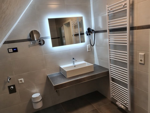 Helles Badezimmer mit Waschbecken, Spiegel und Handtuchheizung in Ferienwohnung Brak.