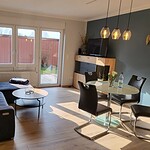 Helles Wohnzimmer mit Sofa, Esstisch und moderner Einrichtung in Ferienwohnung Brak.