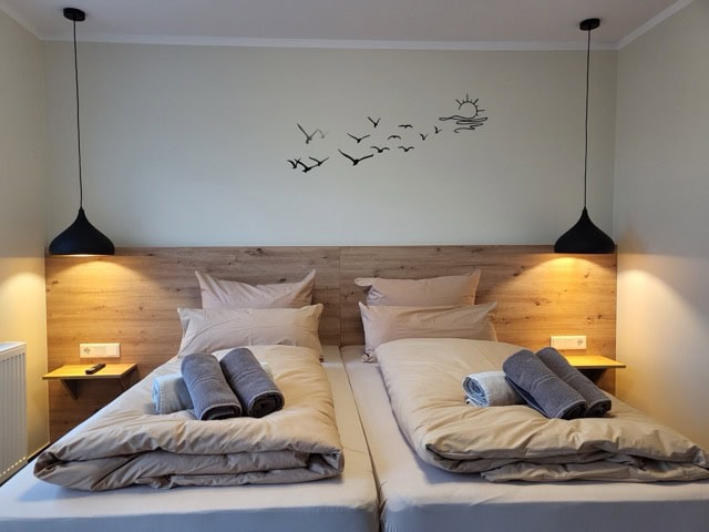 Schlafzimmer mit zwei Betten, Handtüchern und angenehmer Beleuchtung.